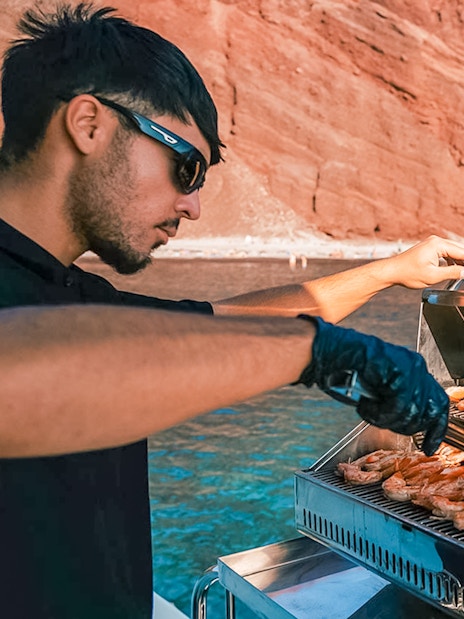 Grilling shrimp on a catamaran with Santorini's red cliffs in the background.