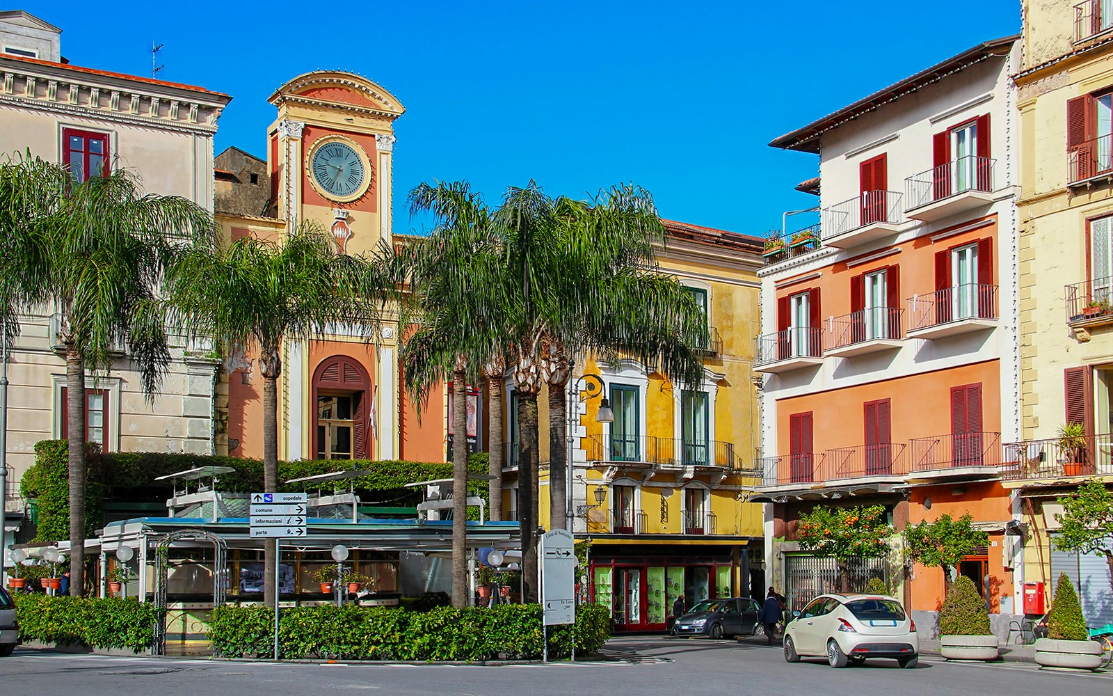 Clock tower and colorful buildings in Sorrento, Italy, with palm trees lining the street.
