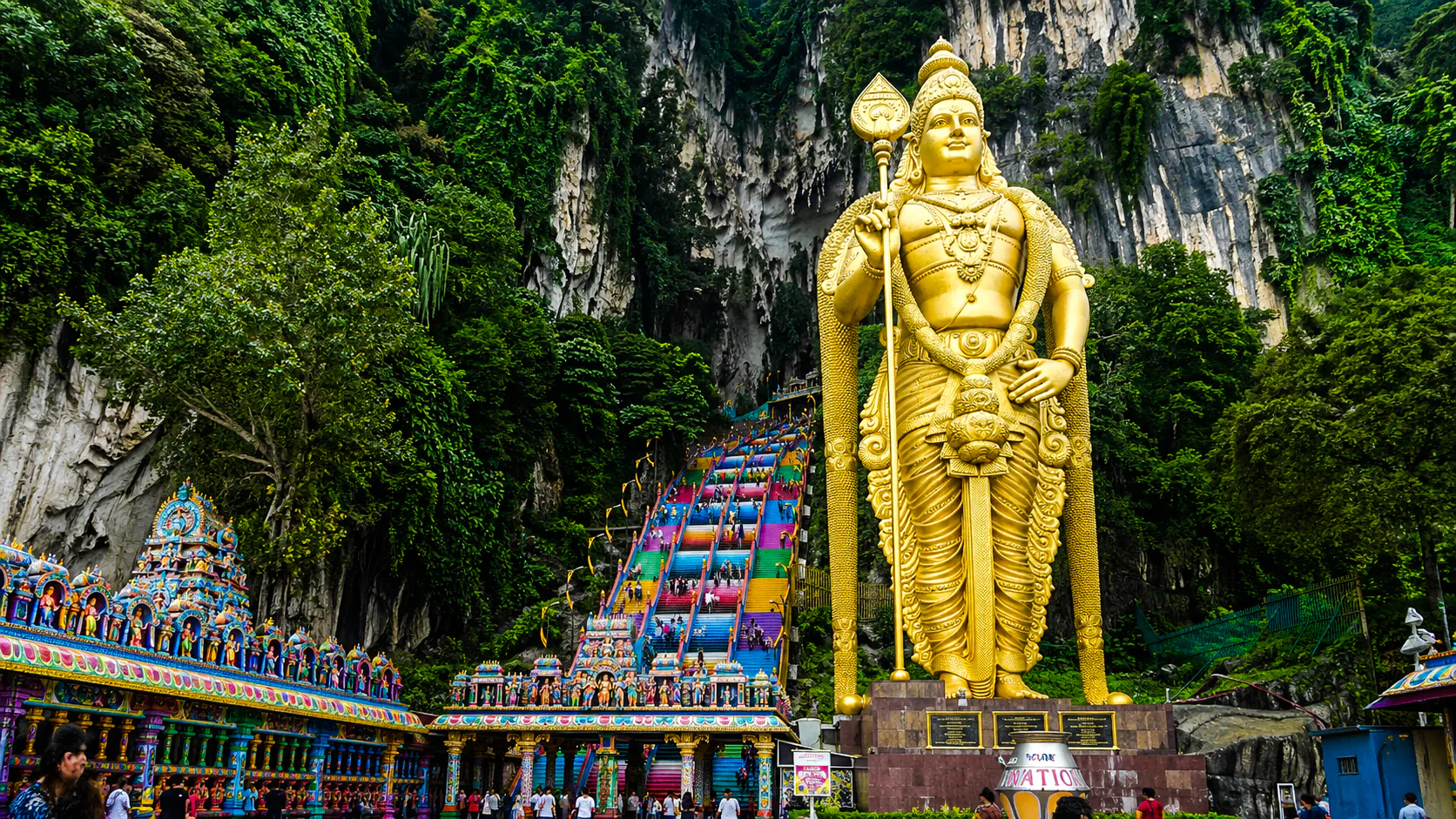 Golden statue of Lord Murugan at Batu Caves entrance with colorful steps, Kuala Lumpur.
