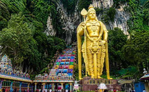 Golden statue of Lord Murugan at Batu Caves entrance with colorful steps, Kuala Lumpur.