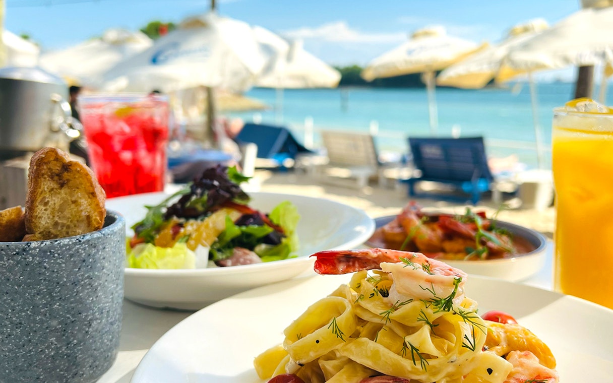 Pasta and salad dishes with drinks by a beachside setting, part of Food Discovery Pass.