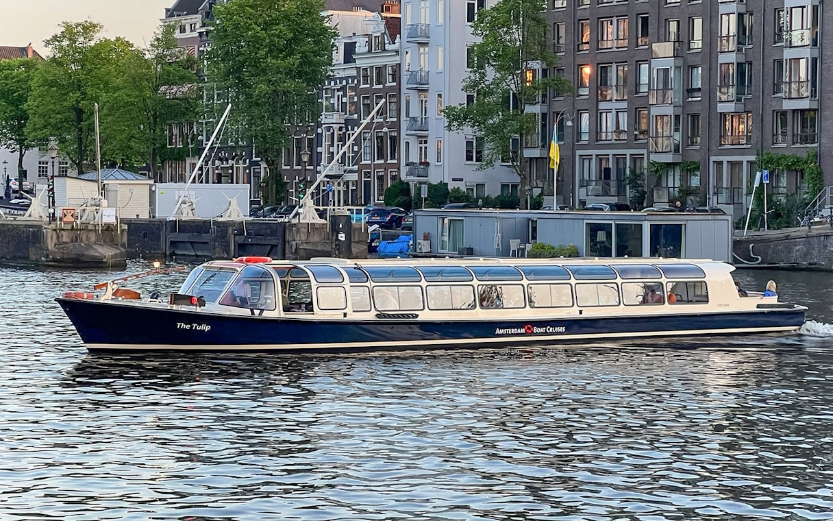 Amsterdam canal cruise boat on water with city buildings in the background.