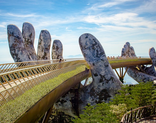 Golden Bridge in Ba Na Hills, Vietnam, with tourists walking across the iconic hand-supported structure.