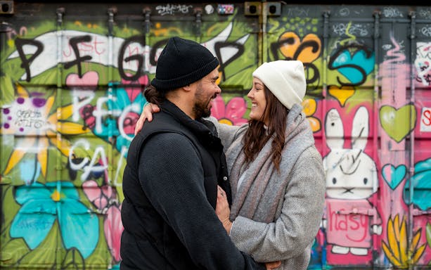Couple smiling in front of colorful graffiti at NDSM, Amsterdam.
