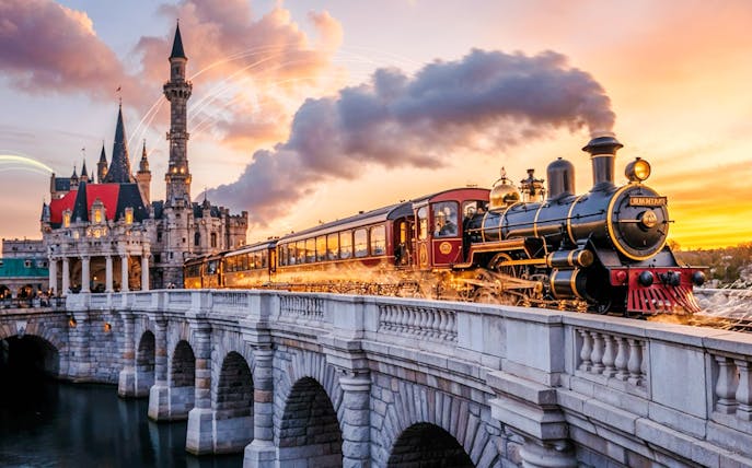 Steam train crossing a bridge towards Disneyland Paris at sunset, France.