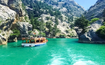 Boat cruising through Green Canyon with rocky cliffs and turquoise water, Alanya tour.