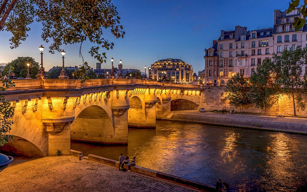 Pont Neuf bridge illuminated at night over the Seine River in Paris.