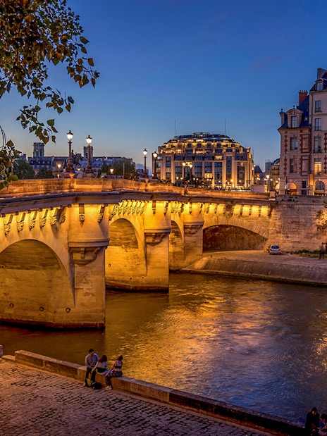 Pont Neuf bridge illuminated at night over the Seine River in Paris.