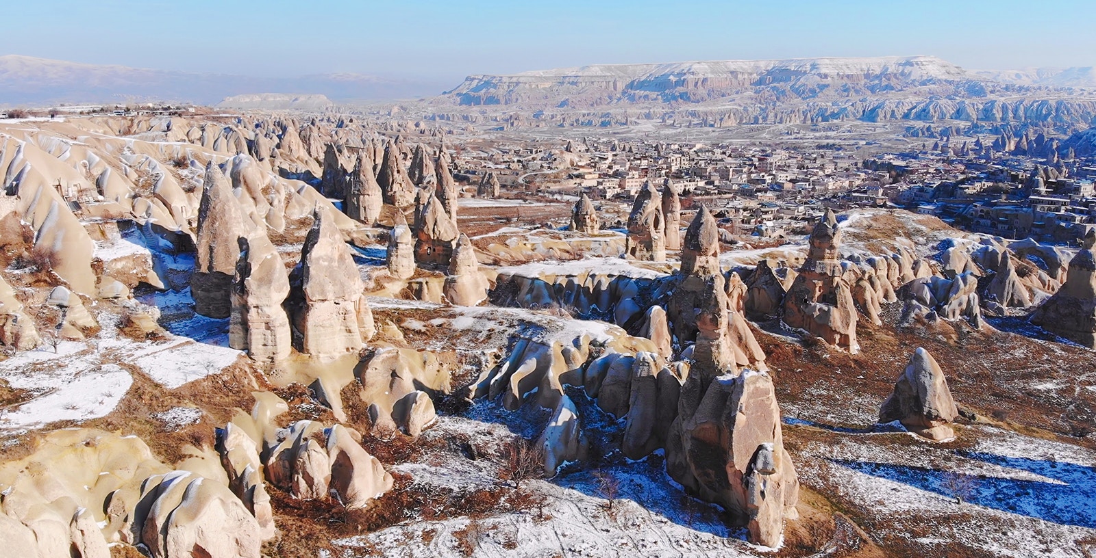 Rock formations in Goreme Valley, Cappadocia, with snow-dusted landscape and distant town view.
