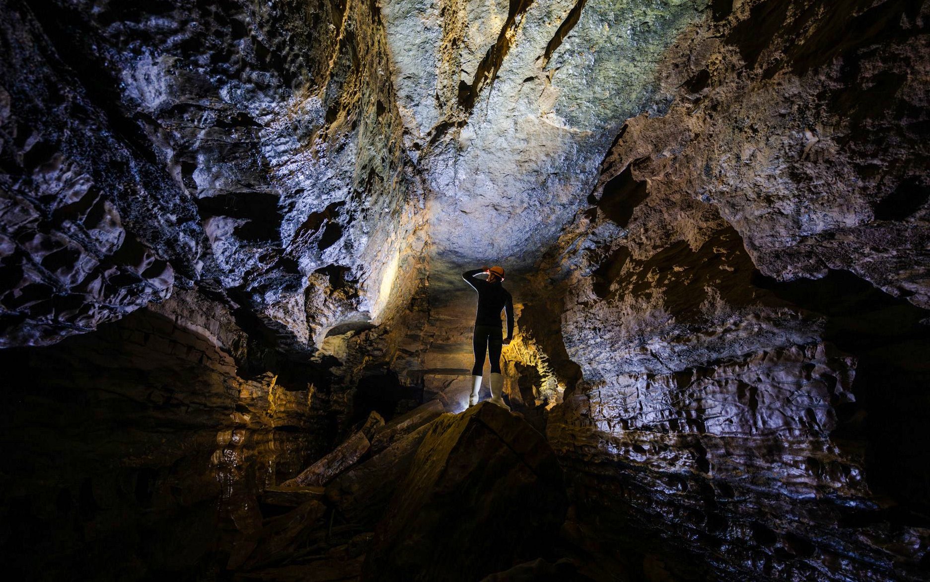 Person exploring Okohua Glowworm Cave, illuminated rock formations above.