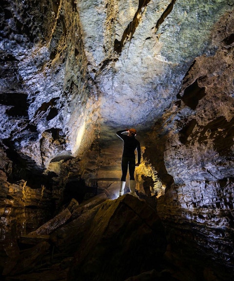 Person exploring Okohua Glowworm Cave, illuminated rock formations above.