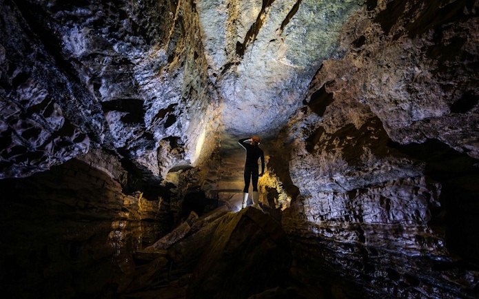 Person exploring Okohua Glowworm Cave, illuminated rock formations above.