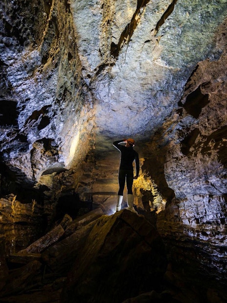 Person exploring Okohua Glowworm Cave, illuminated rock formations above.