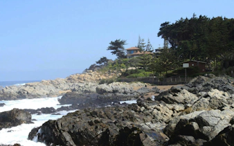 Rocky coastline near Pablo Neruda's house with ocean waves and coastal trees.