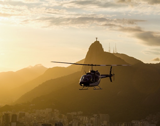 Helicopter flying over Rio de Janeiro with Christ the Redeemer statue in the background at sunset.
