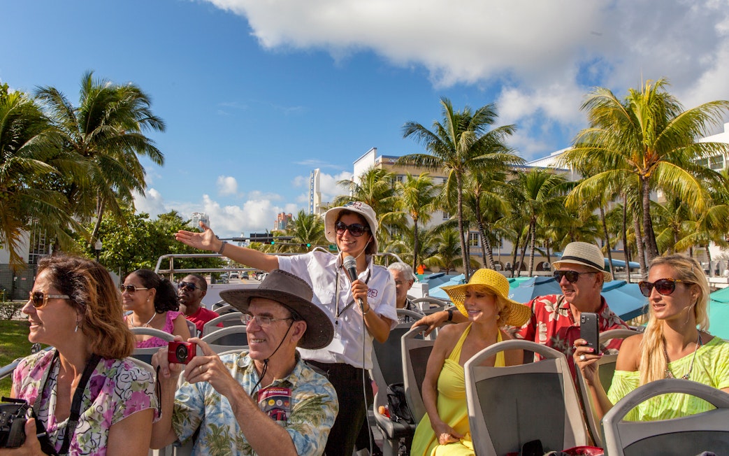 Group enjoying a guided tour on a Hop On Hop Off bus in Miami with palm trees in the background.