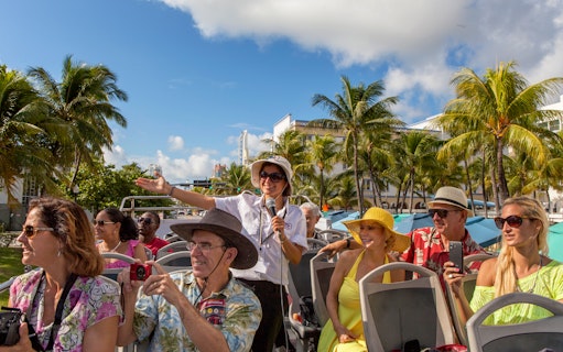 Group enjoying a guided tour on a Hop On Hop Off bus in Miami with palm trees in the background.