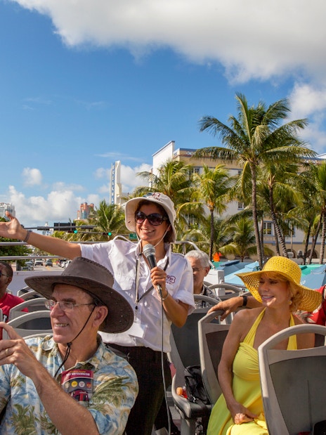 Group enjoying a guided tour on a Hop On Hop Off bus in Miami with palm trees in the background.