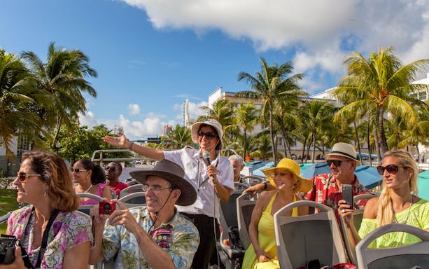 Group enjoying a guided tour on a Hop On Hop Off bus in Miami with palm trees in the background.