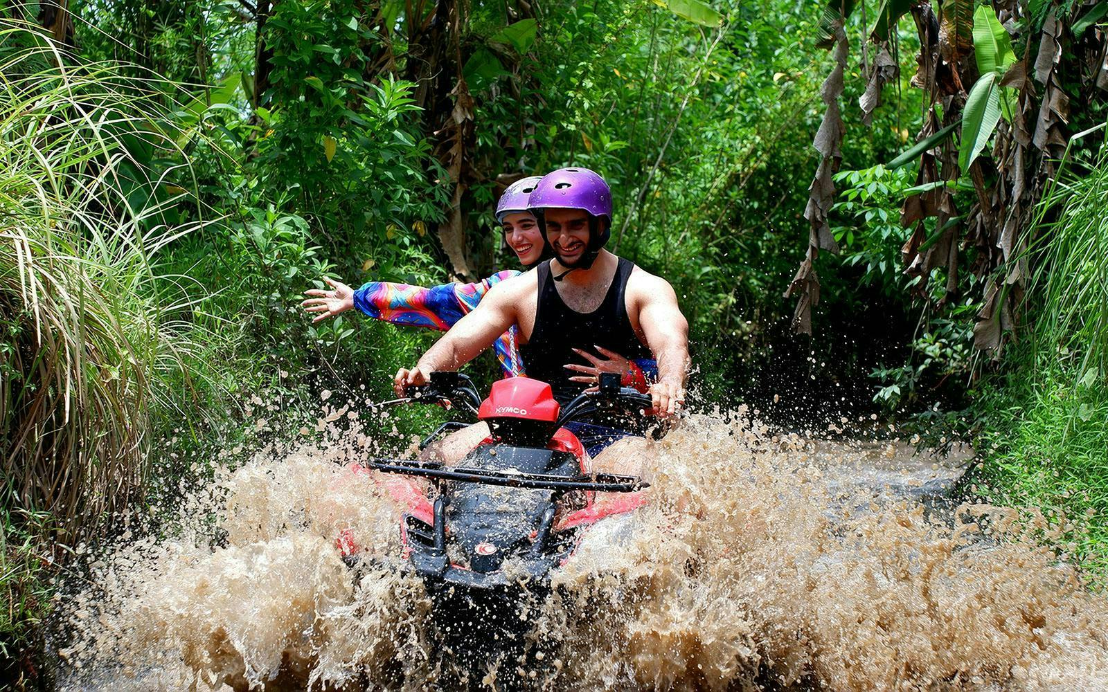 Couple riding quad bike through muddy trail in Bali jungle.