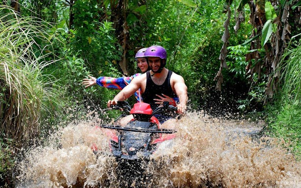 Couple riding quad bike through muddy trail in Bali jungle.