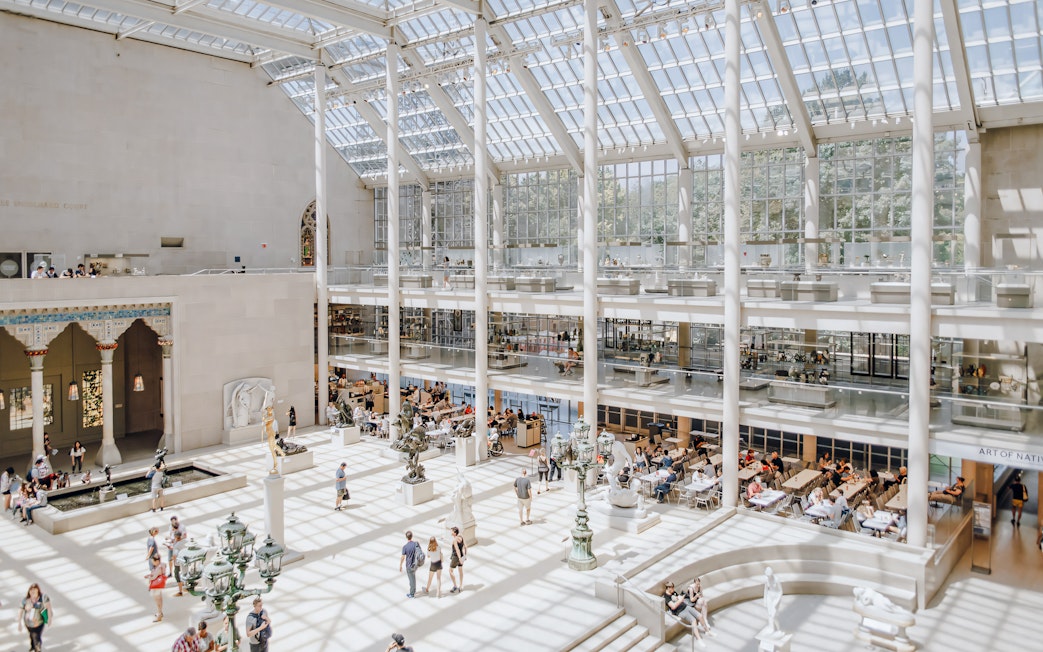Metropolitan Museum of Art skylit atrium with visitors and sculptures.