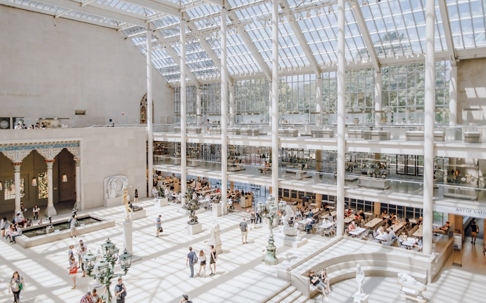 Metropolitan Museum of Art skylit atrium with visitors and sculptures.
