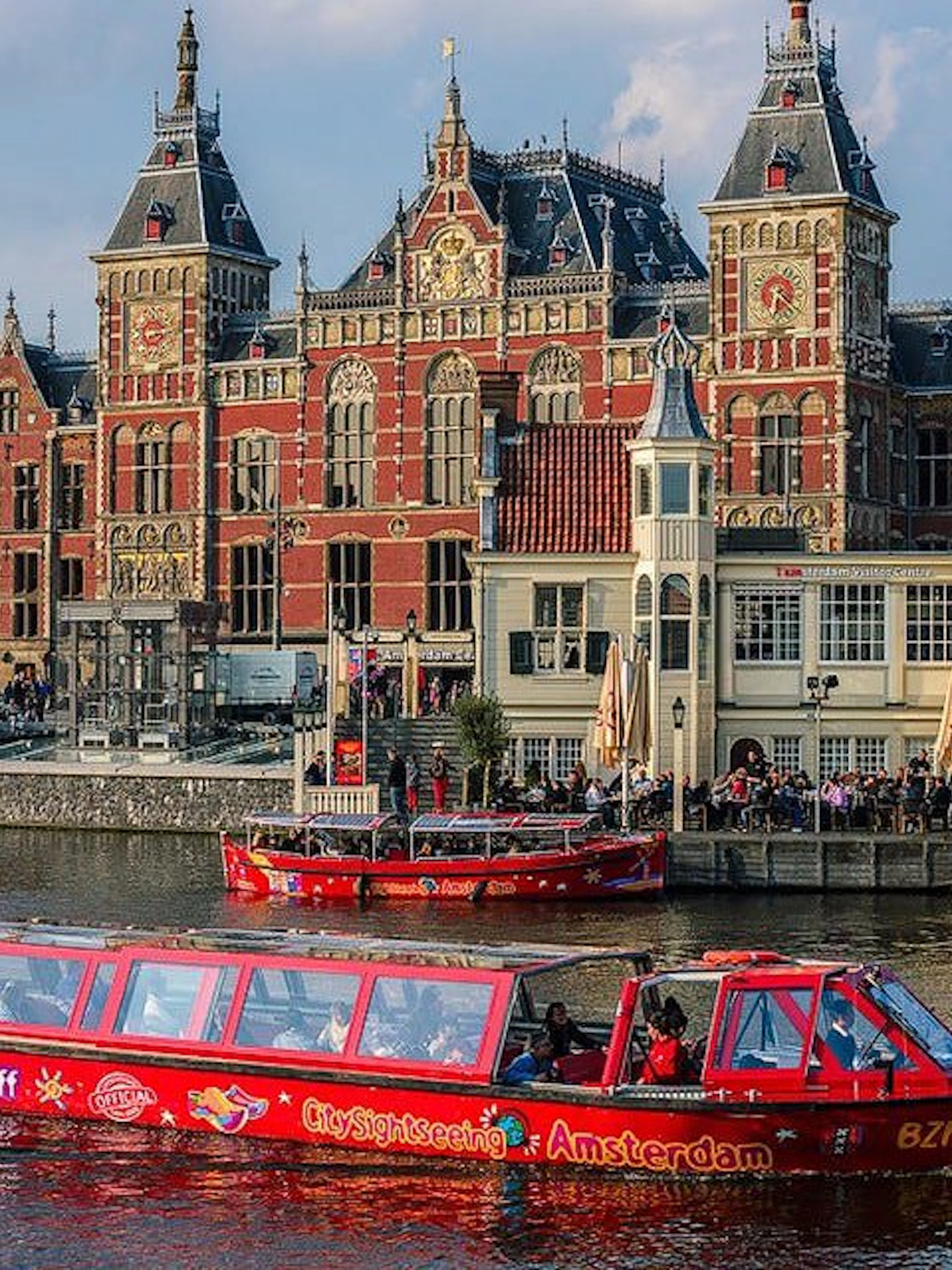 City Sightseeing Amsterdam boat near historic building on canal.