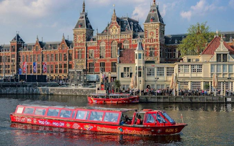 City Sightseeing Amsterdam boat near historic building on canal.