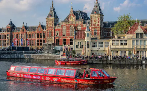 City Sightseeing Amsterdam boat near historic building on canal.