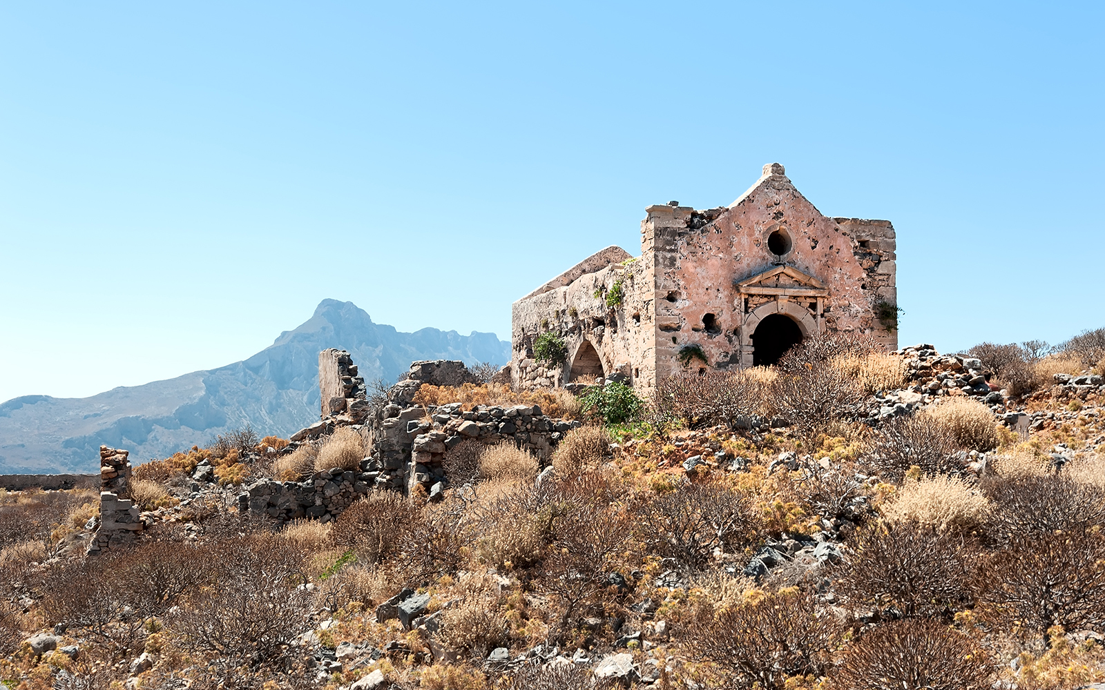 Ruined Venetian fortress church with mountain backdrop, Crete, Greece.