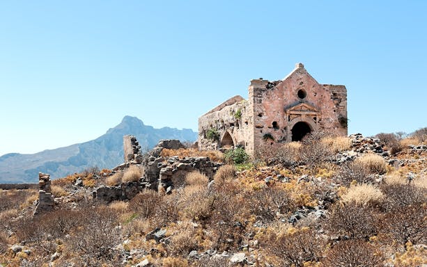Ruined Venetian fortress church with mountain backdrop, Crete, Greece.