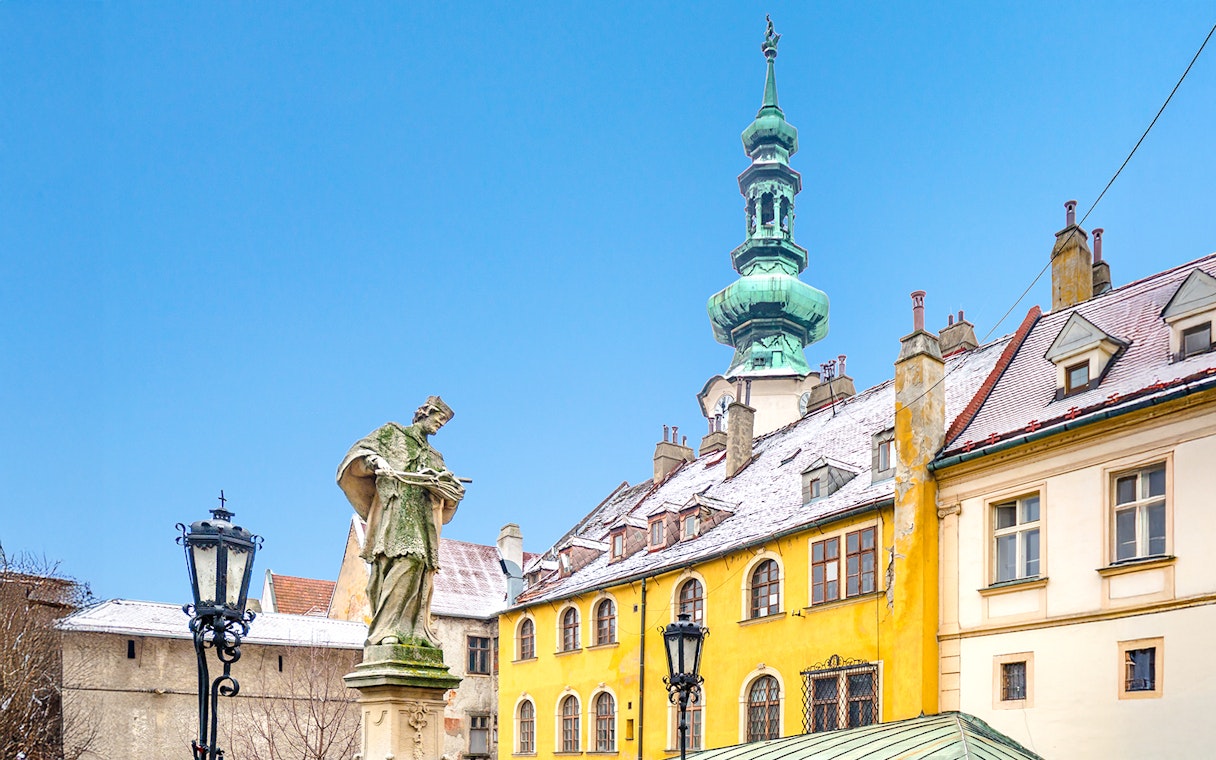 Michael's Gate in Bratislava with snow-covered rooftops and a statue in winter.