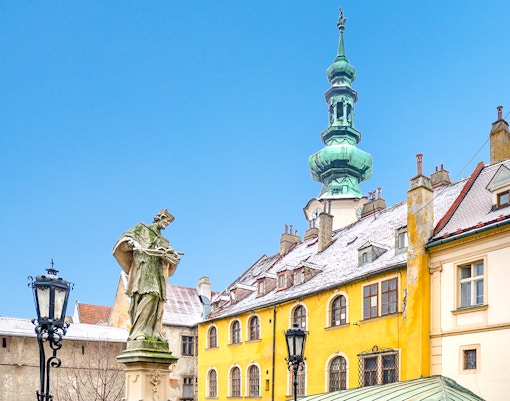 Michael's Gate in Bratislava with snow-covered rooftops and a statue in winter.