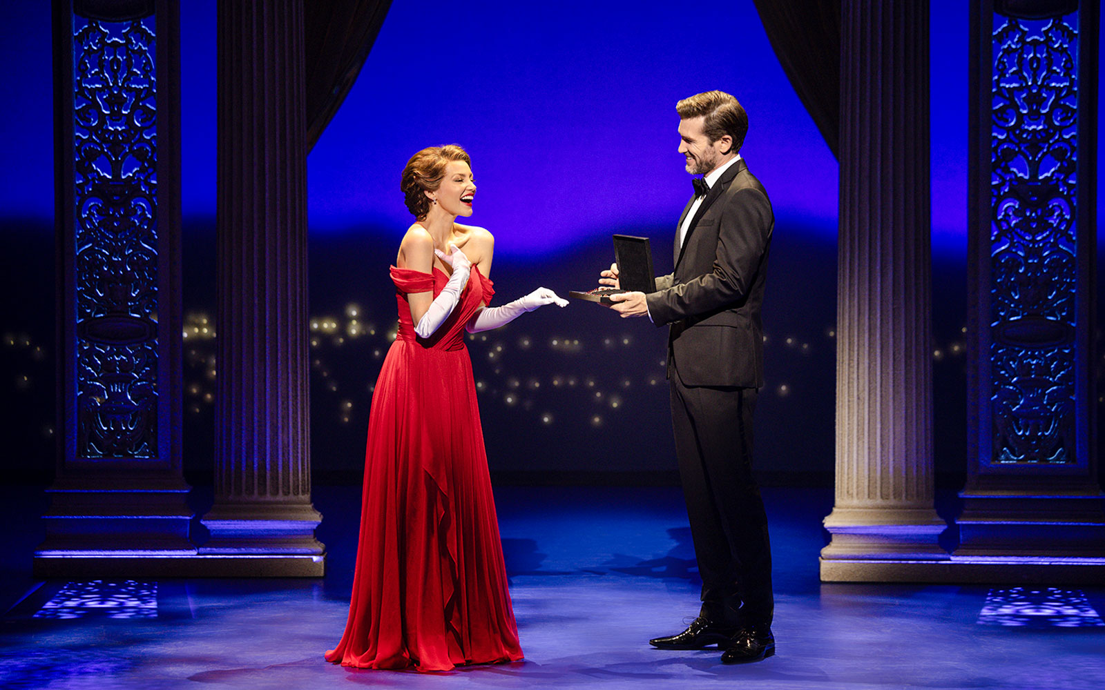 Cast performing a scene from Pretty Woman The Musical with ornate columns and blue lighting.