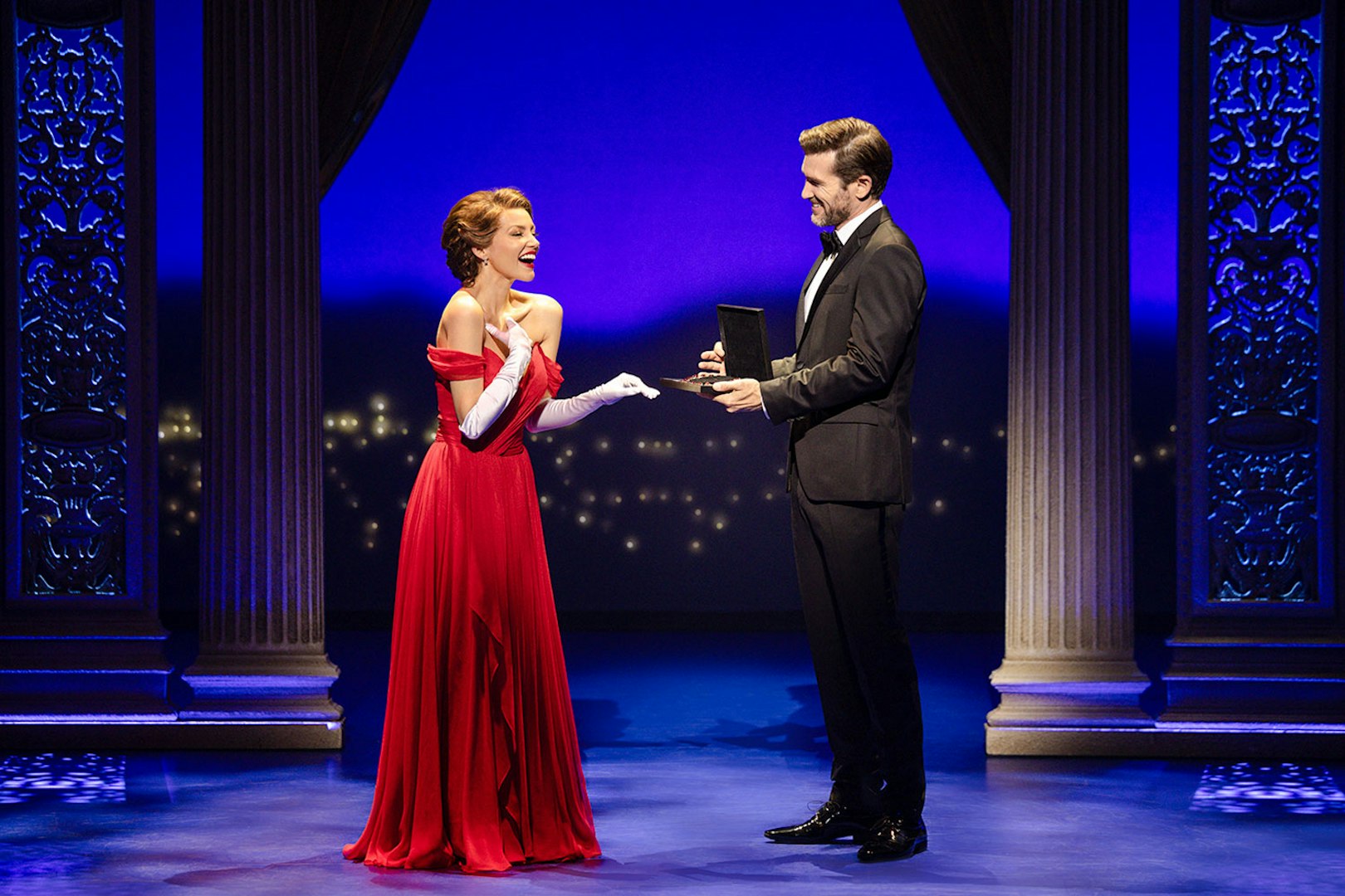 Cast performing a scene from Pretty Woman The Musical with ornate columns and blue lighting.