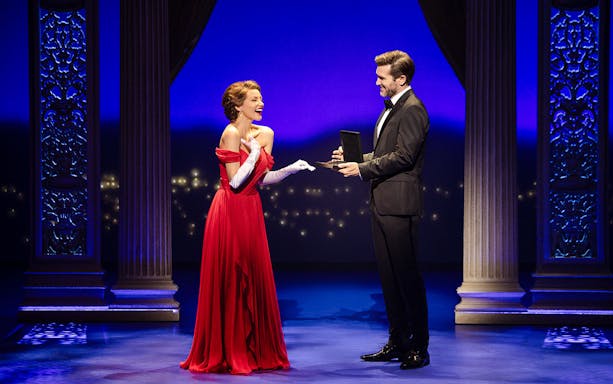 Cast performing a scene from Pretty Woman The Musical with ornate columns and blue lighting.