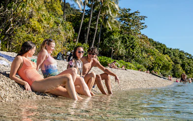 People relaxing on a pebble beach at Fitzroy Island, surrounded by lush greenery and clear water.