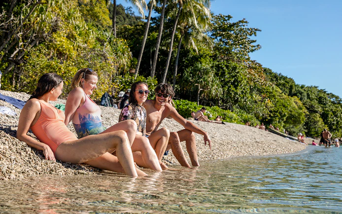 People relaxing on a pebble beach at Fitzroy Island, surrounded by lush greenery and clear water.