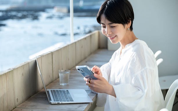 Person using smartphone and laptop by the sea, illustrating Japan Unlimited Pocket WiFi Rental.