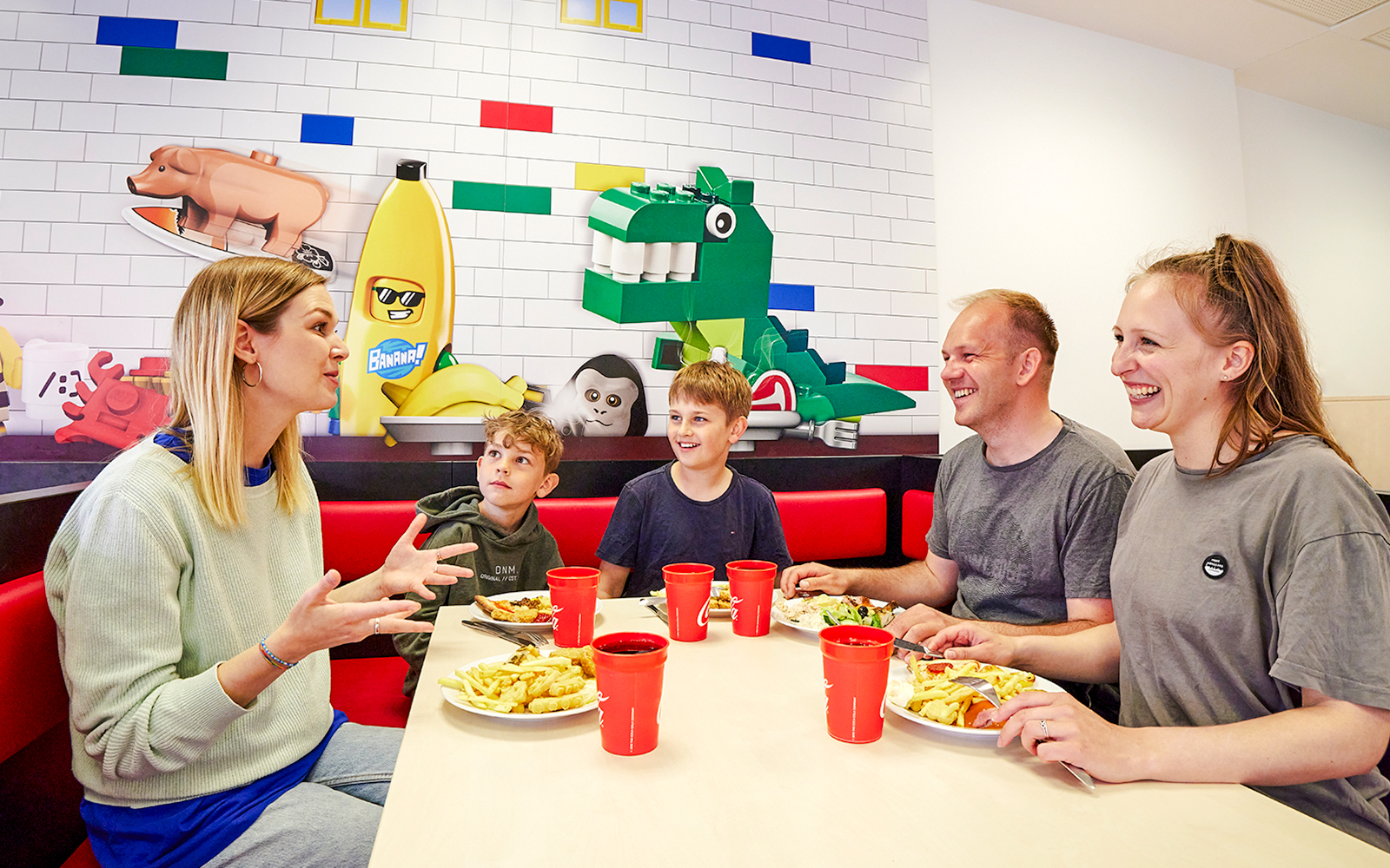 Family dining at a cafe in LEGOLAND Billund with LEGO-themed wall art.