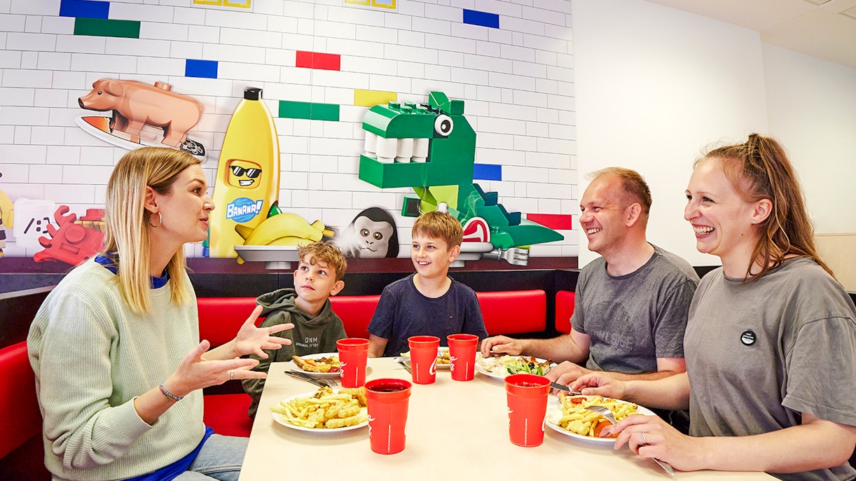 Family dining at a cafe in LEGOLAND Billund with LEGO-themed wall art.