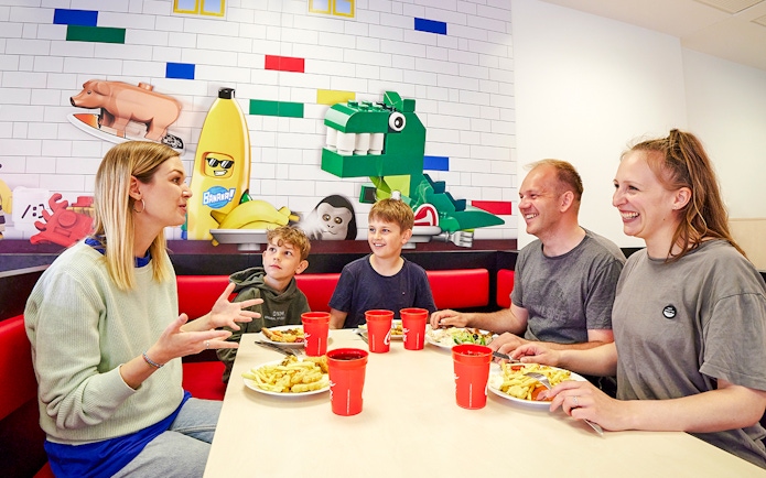 Family dining at a cafe in LEGOLAND Billund with LEGO-themed wall art.