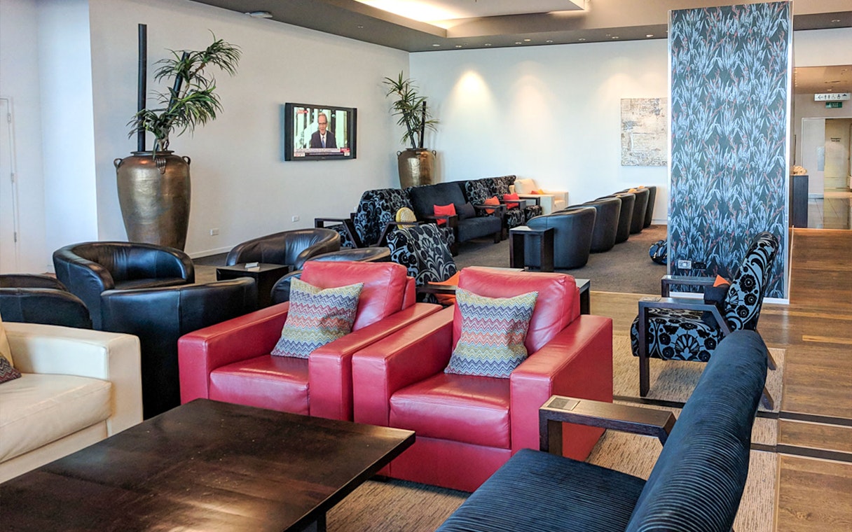 Plaza Premium Lounge seating area with red and black chairs, TV, and decorative plants.