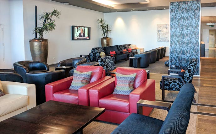 Plaza Premium Lounge seating area with red and black chairs, TV, and decorative plants.