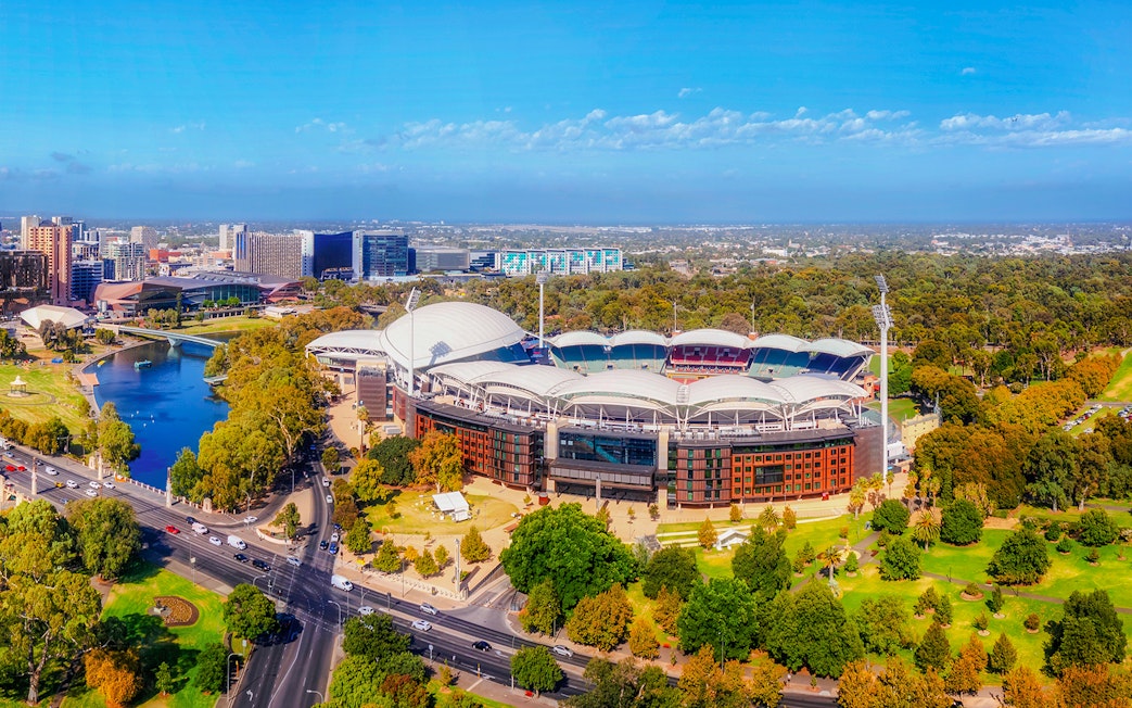 Aerial view of Adelaide Oval Stadium surrounded by parkland and cityscape.