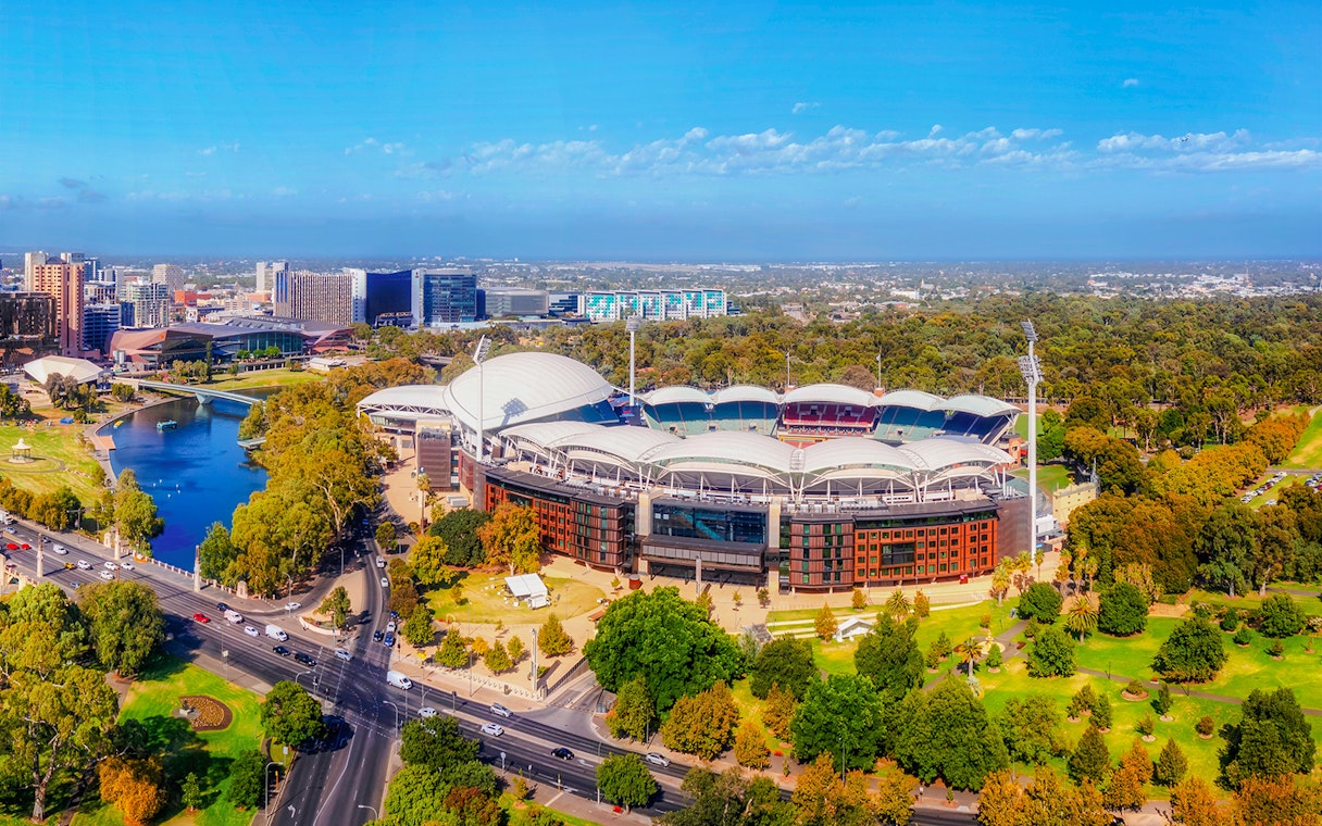 Aerial view of Adelaide Oval Stadium surrounded by parkland and cityscape.