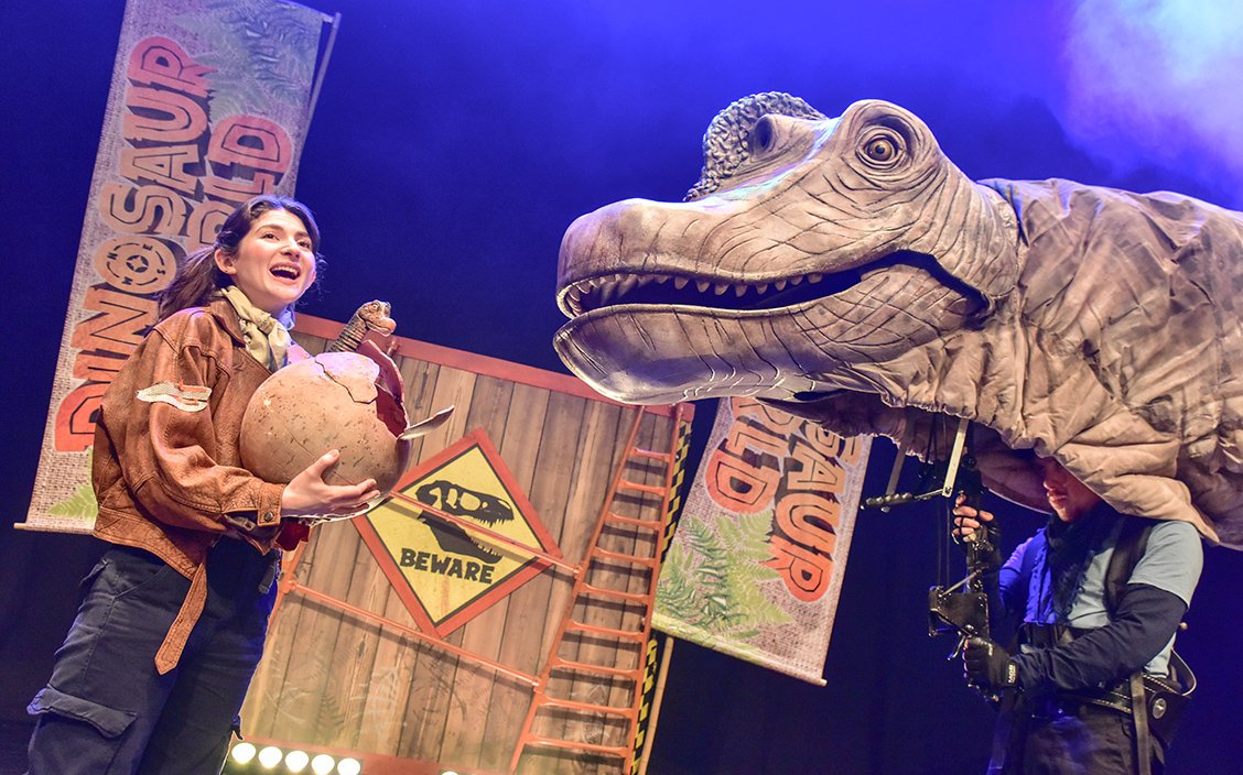 Performer with dinosaur puppet on stage at Dinosaur World Live, West End.