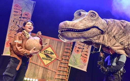 Performer with dinosaur puppet on stage at Dinosaur World Live, West End.