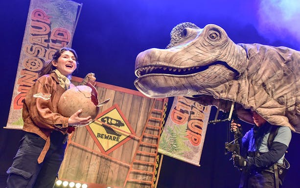 Performer with dinosaur puppet on stage at Dinosaur World Live, West End.